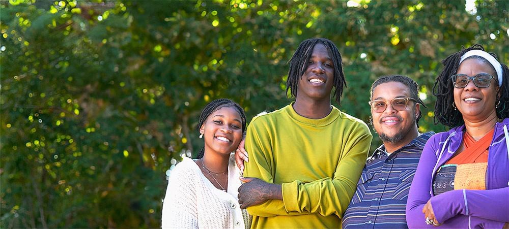 Two parents and two teenagers smile together in a park.